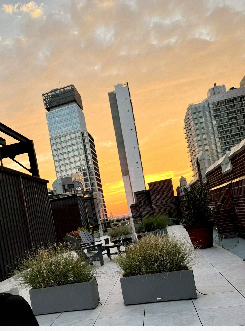 Rooftop tables and chairs at sunset with residents gathered, planters and skyline beyond